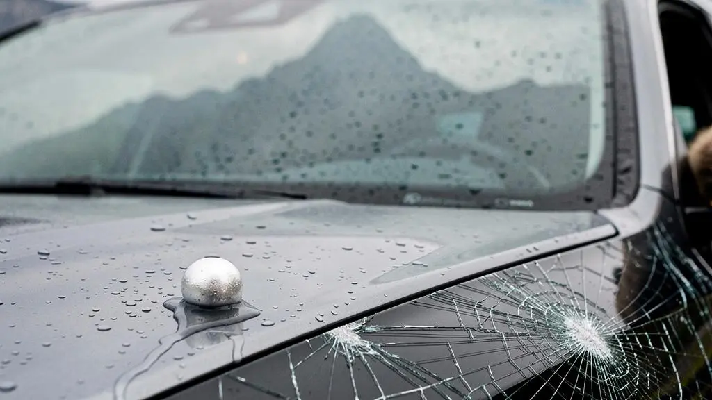 Pare-brise fissuré d'une voiture suisse avec un grêlon posé sur le capot, symbolisant les risques couverts par la casco partielle